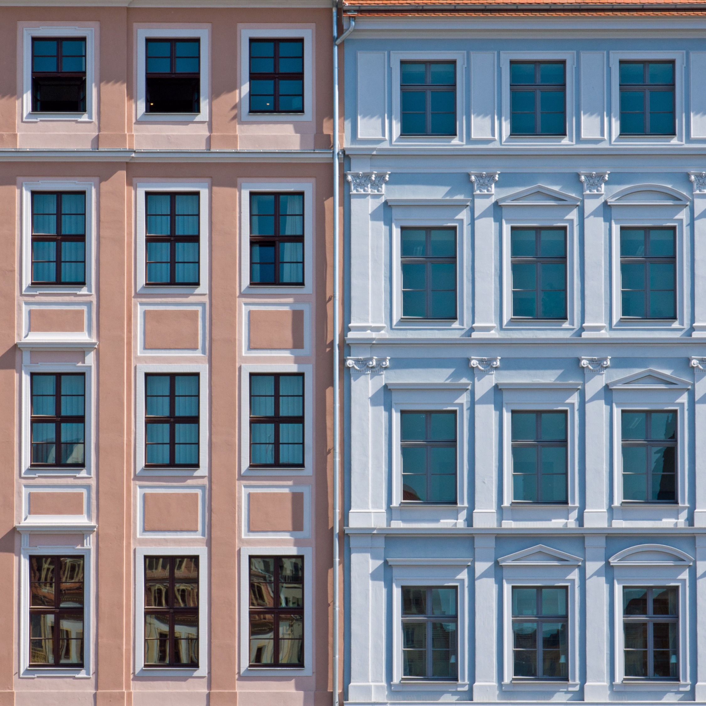 Fassade von zwei benachbarten Wohnhäusern in Rosa und Hellblau mit vielen Fenstern.