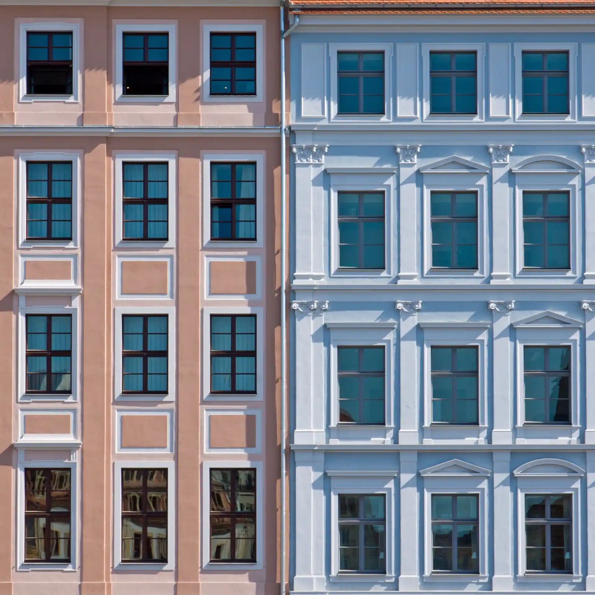 Fassade von zwei benachbarten Wohnhäusern in Rosa und Hellblau mit vielen Fenstern.