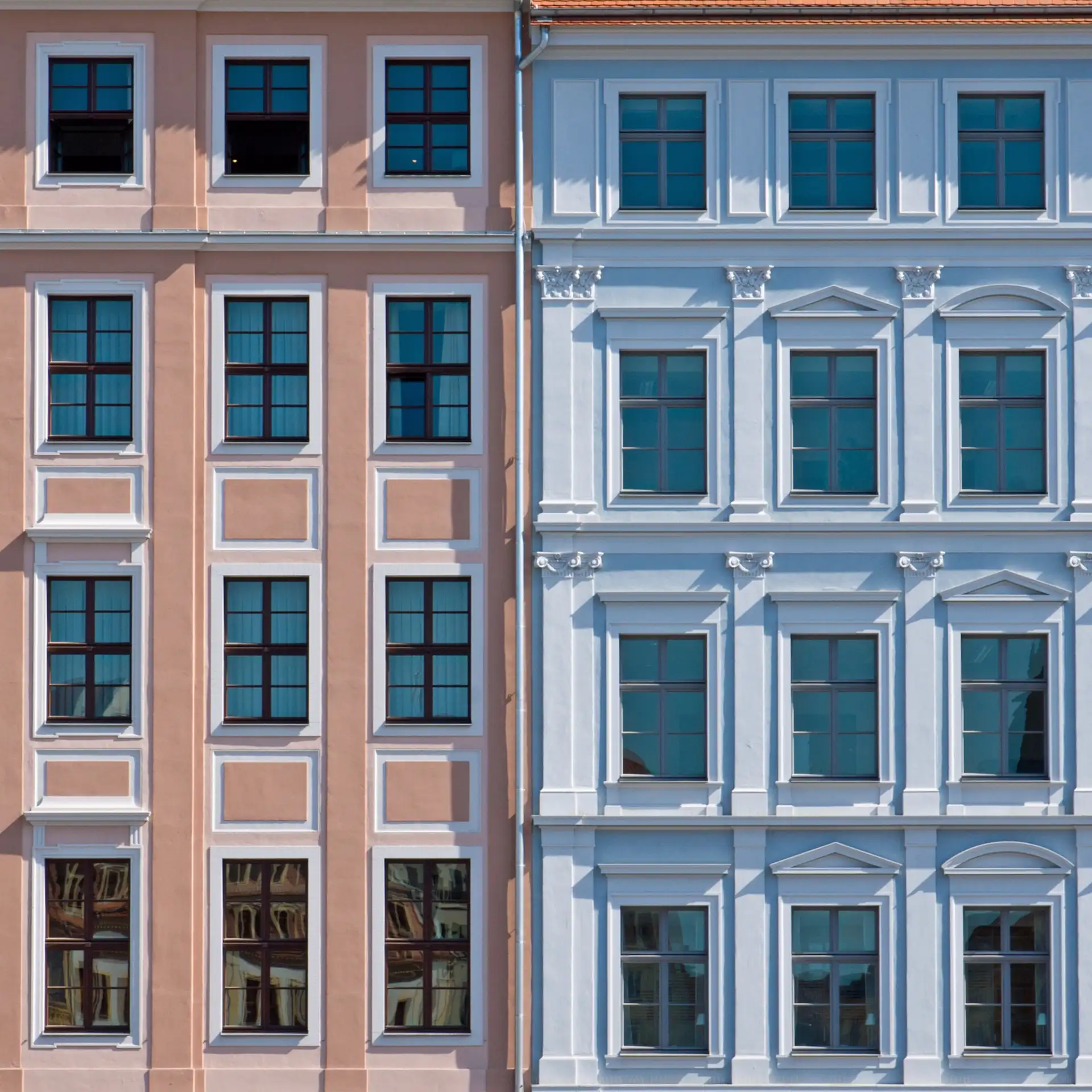Fassade von zwei benachbarten Wohnhäusern in Rosa und Hellblau mit vielen Fenstern.