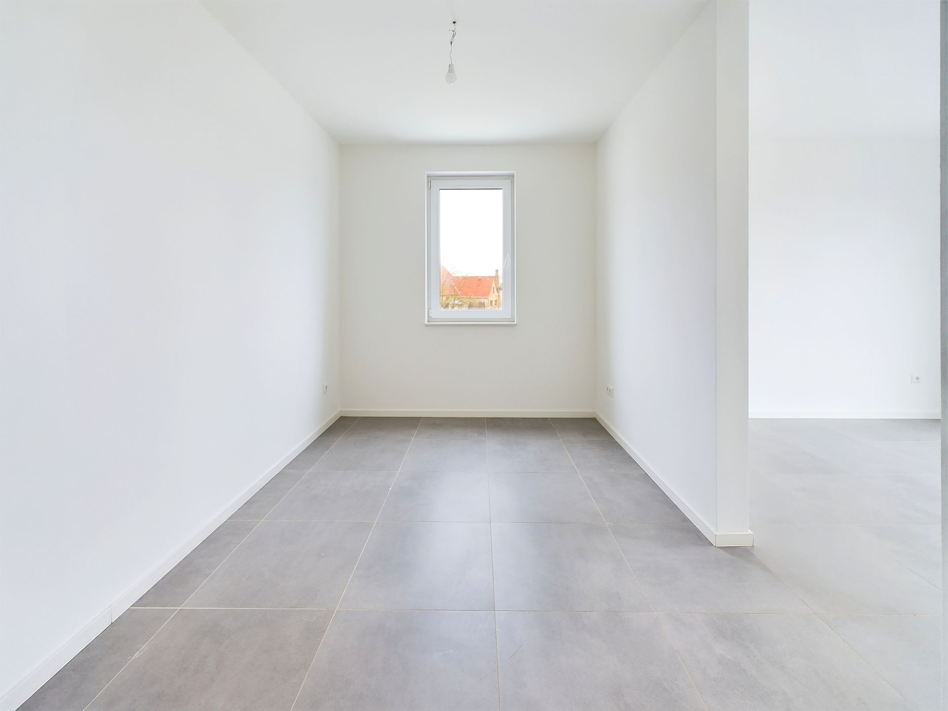 Leerer, heller Raum mit grauen Fliesen und einem Fenster in der Mitte der Rückwand.