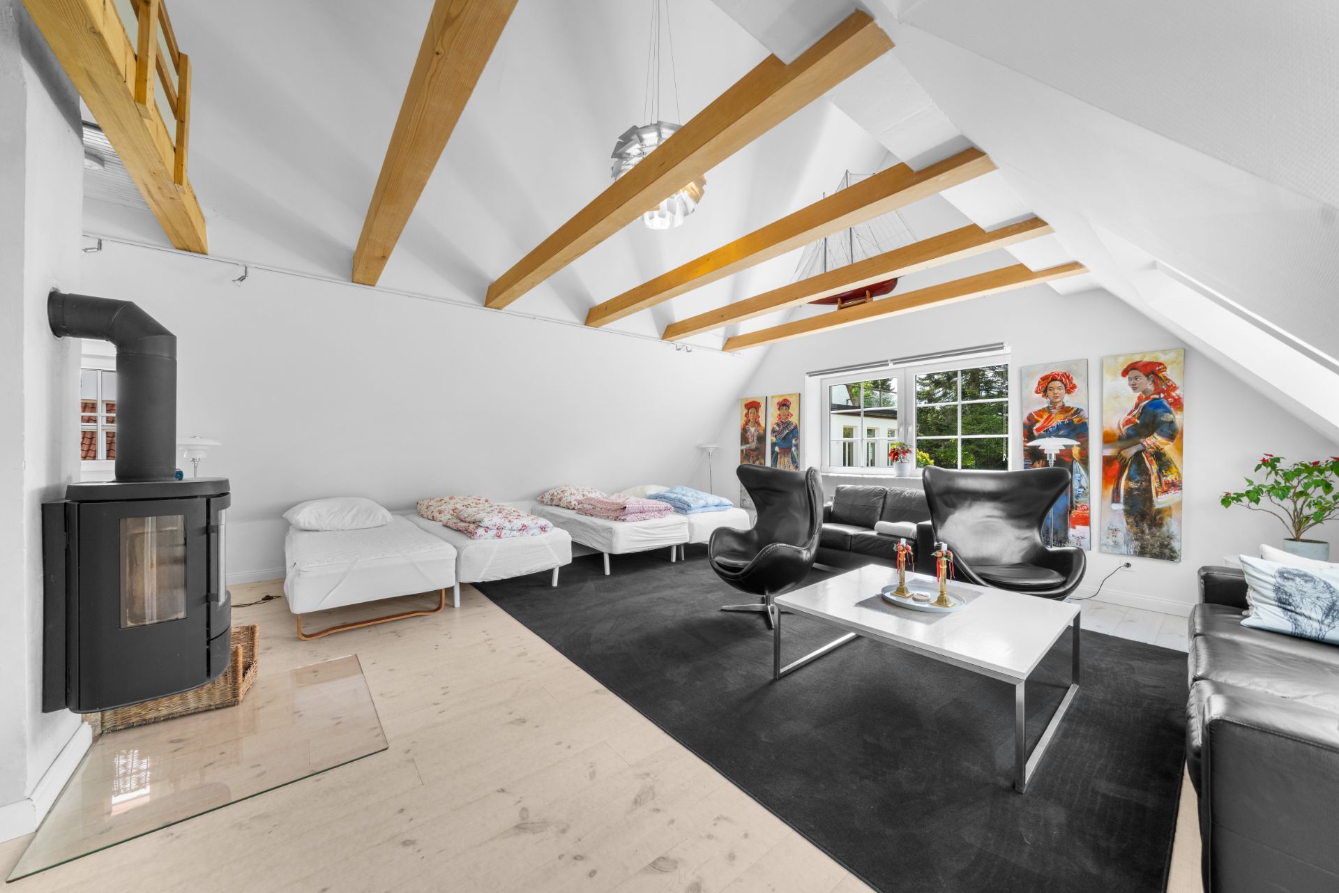 Helles Wohnzimmer mit Holzbalken, Kamin, zwei Betten, Sofa, Sesseln und Gemälden an der Wand.