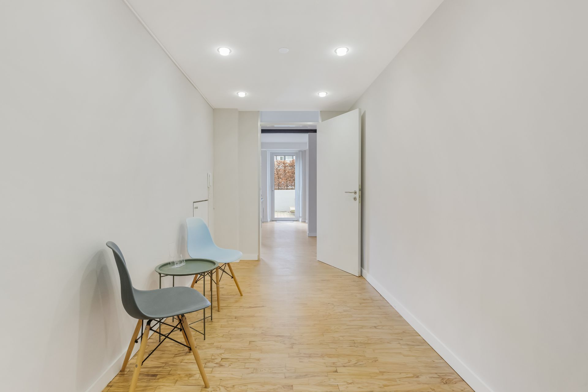 Heller Flur mit Holzfußboden, zwei Stühlen und kleinem Tisch an der Wand.