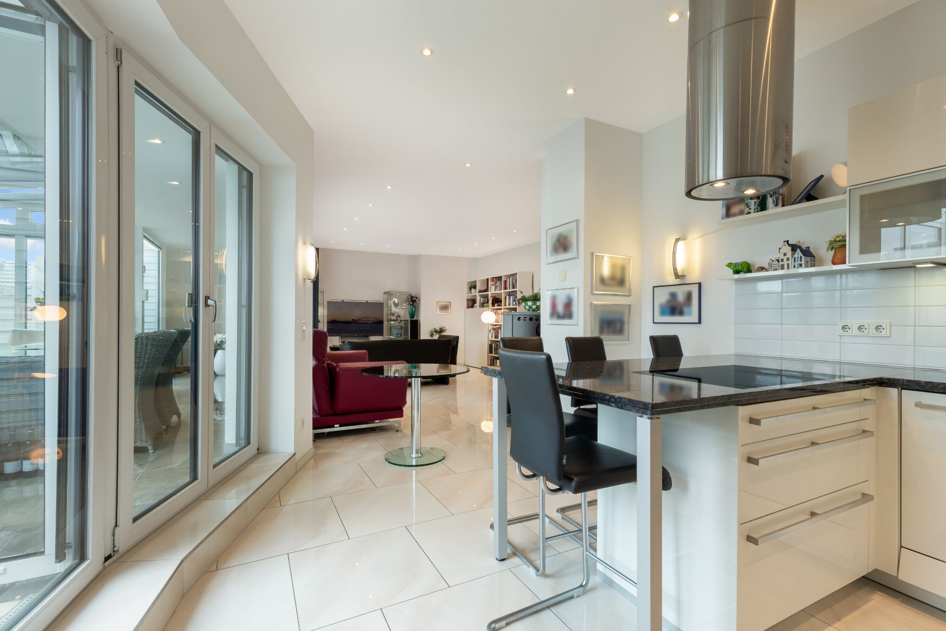 Moderne Wohnküche mit Barhockern, Esstisch, Glasfront und Blick ins Wohnzimmer.