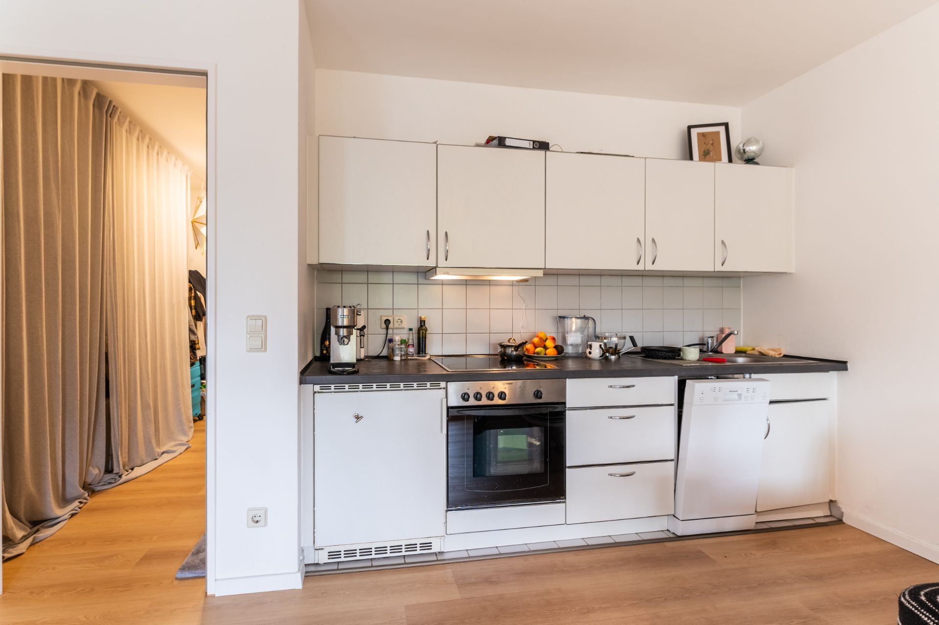 Moderne Einbauküche mit weißen Schränken, Herd, Spüle und Geschirrspüler in einem Wohnraum.