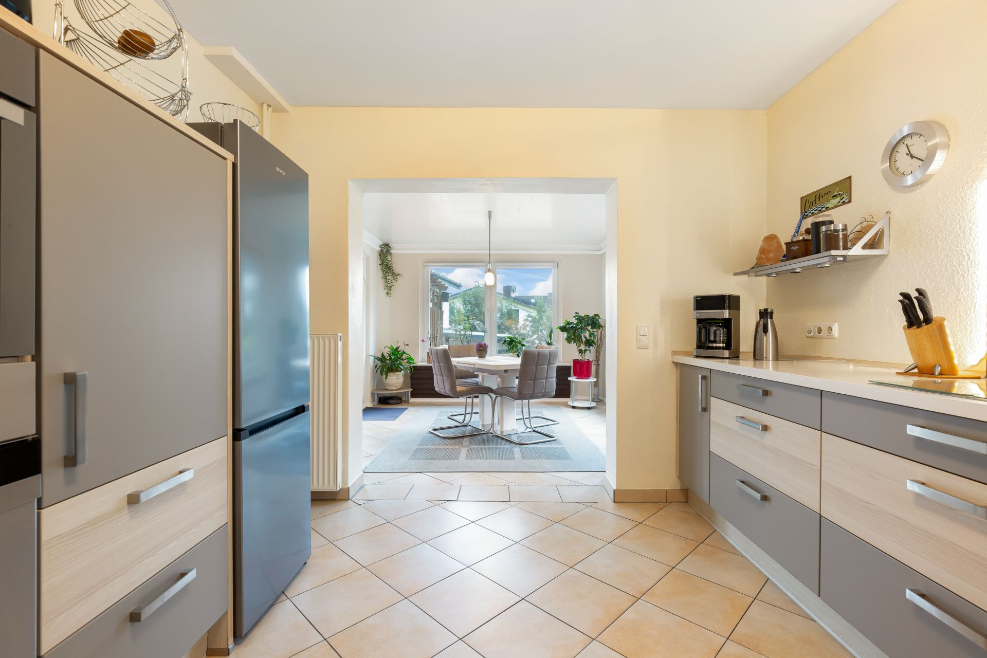 Moderne Küche mit grauen Schränken und Blick auf einen hellen Essbereich mit großen Fenstern.