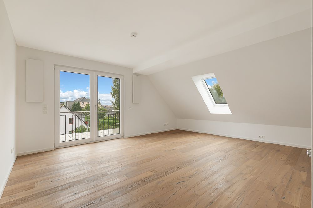 Helles, leeres Zimmer mit Holzfußboden, großer Fensterfront und Dachfenster.