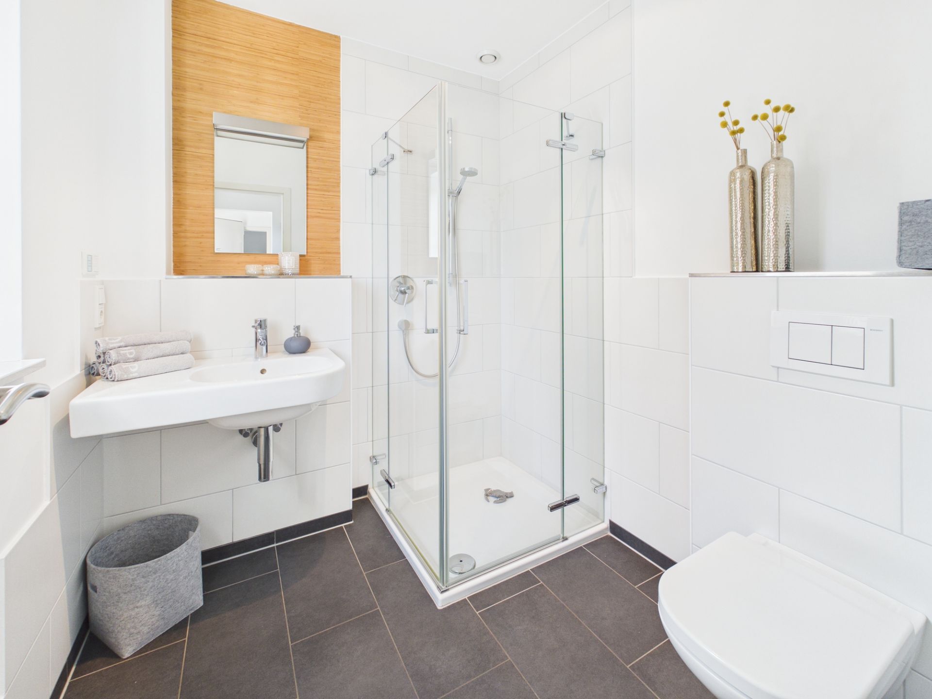 Helles Badezimmer mit Glasdusche, Waschbecken, WC und Dekovasen auf einer Ablage.