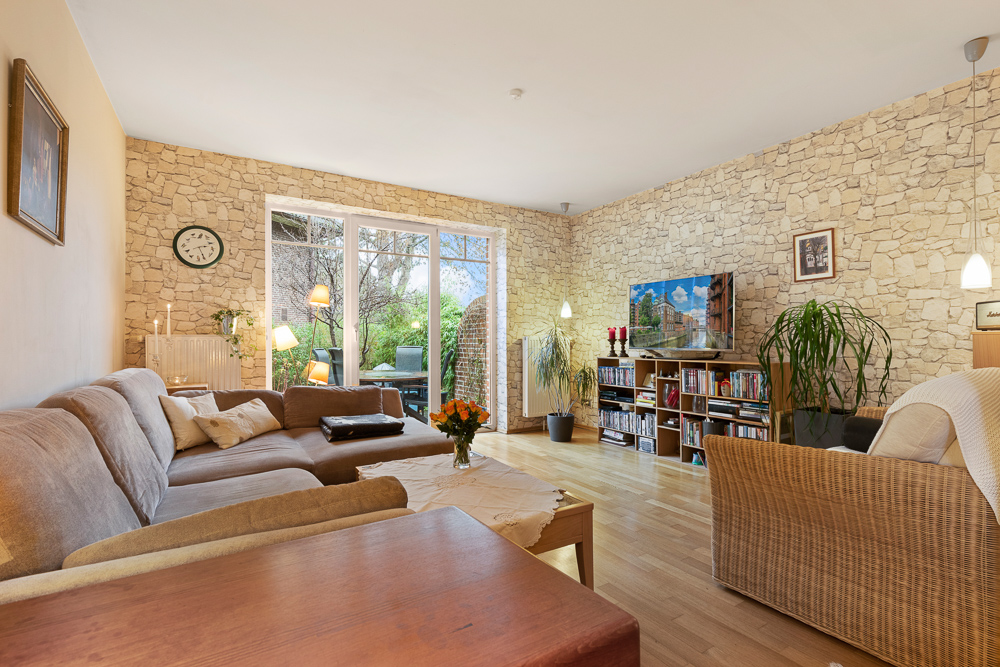 Helles Wohnzimmer mit Steinwand, Sofa, Couchtisch, Fernseher und Zugang zur Terrasse.