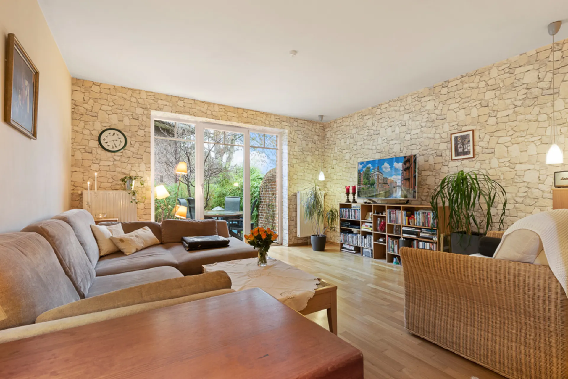Helles Wohnzimmer mit Steinwand, Sofa, Couchtisch, Fernseher und Zugang zur Terrasse.