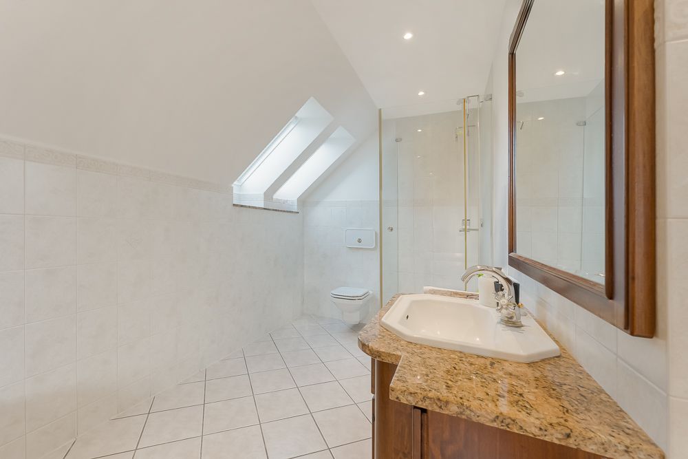 Modernes Badezimmer mit Waschbecken, großem Spiegel, Dusche, WC und Dachfenstern.