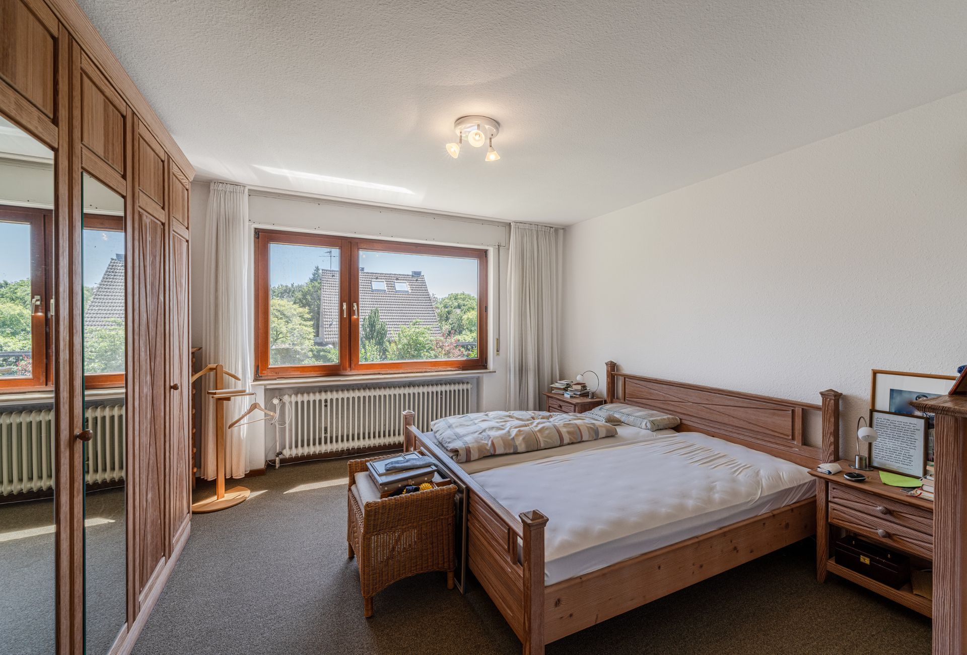 Helles Schlafzimmer mit großem Fenster, Holzbett, Nachttisch und Kleiderschrank.