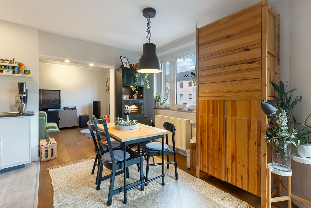 Essbereich mit Holztisch, schwarzen Stühlen, großen Fenstern und Holzschrank in heller Wohnung.