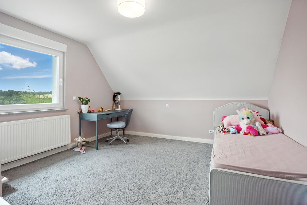 Helles Kinderzimmer mit Schreibtisch, Stuhl und Bett mit Kuscheltieren unter Dachschräge.
