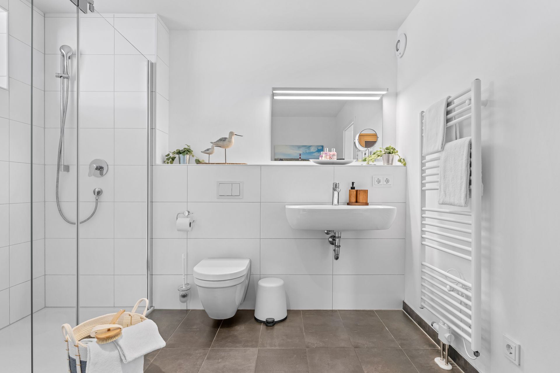 Modernes Bad mit ebenerdiger Dusche, WC, Waschbecken, Handtuchheizkörper und großem Spiegel.