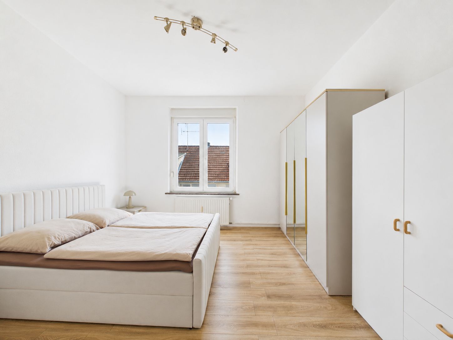 Helles Schlafzimmer mit Doppelbett, weißen Schränken und Holzfußboden.