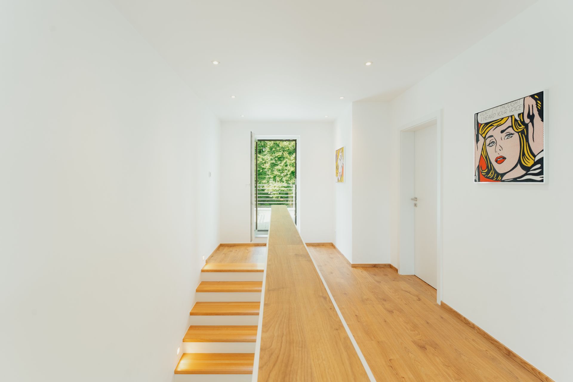Heller Flur mit Holztreppe, Holzfußboden und Pop-Art-Gemälden an weißen Wänden.
