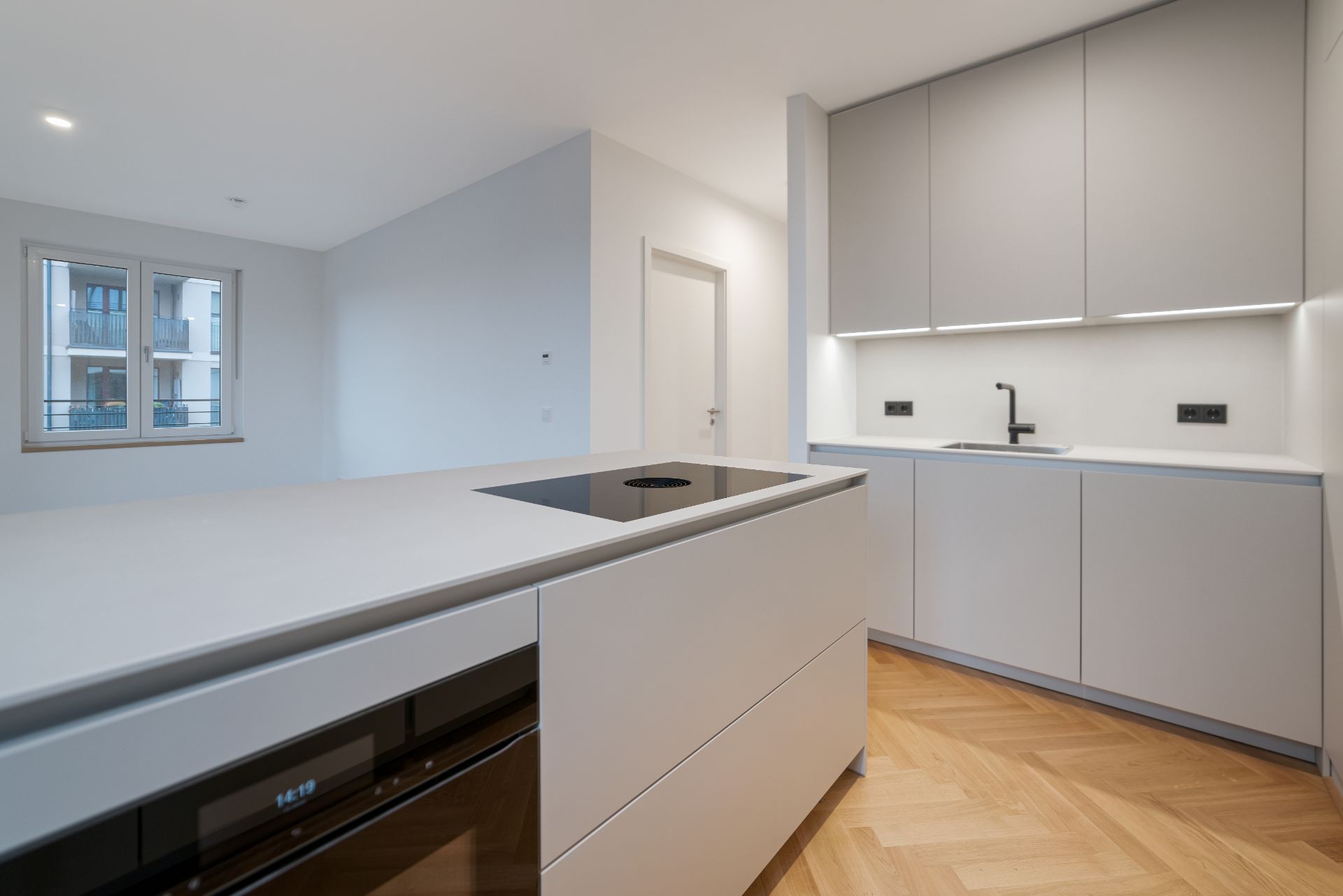 Moderne, helle Küche mit Kochinsel, Einbauschränken und Parkettboden.
