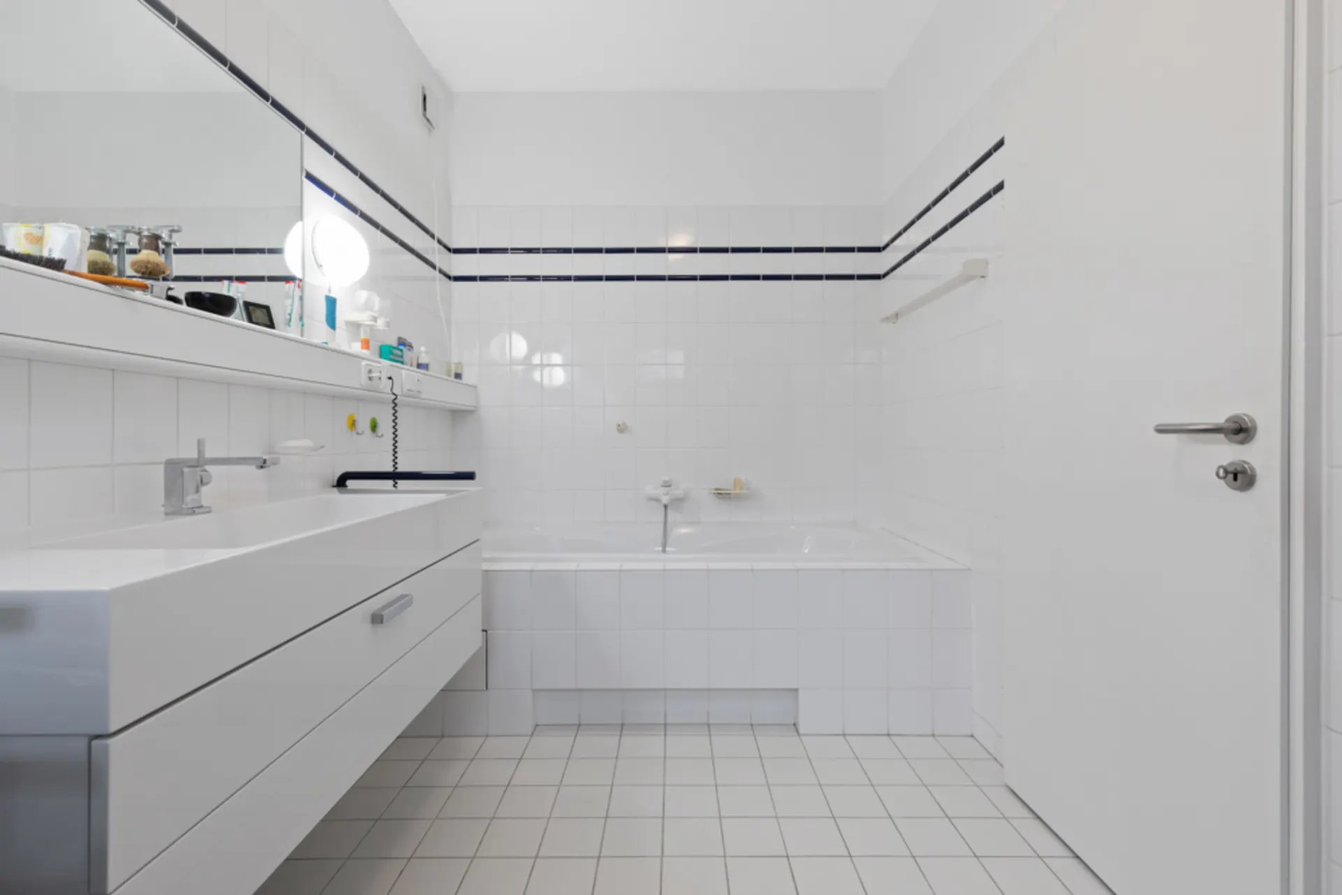 Modernes Badezimmer mit weißer Fliesenwand, Badewanne und breitem Waschbecken mit Spiegel.