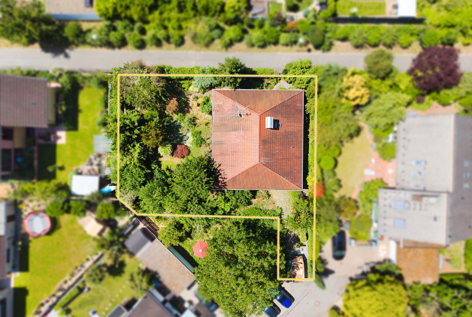Luftaufnahme eines Einfamilienhauses mit rotem Dach und großem, grünen Garten, von oben gesehen.