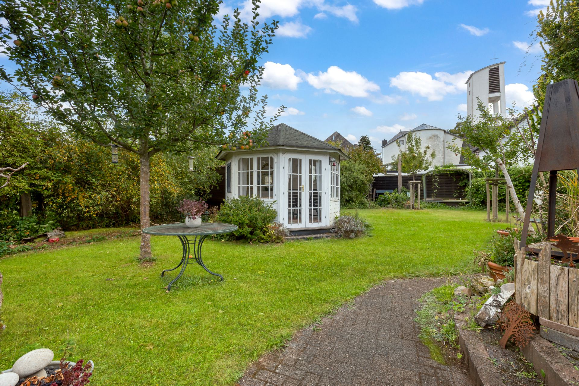 Grüner Garten mit rundem Pavillon, Baum, rundem Tisch und gepflastertem Weg.