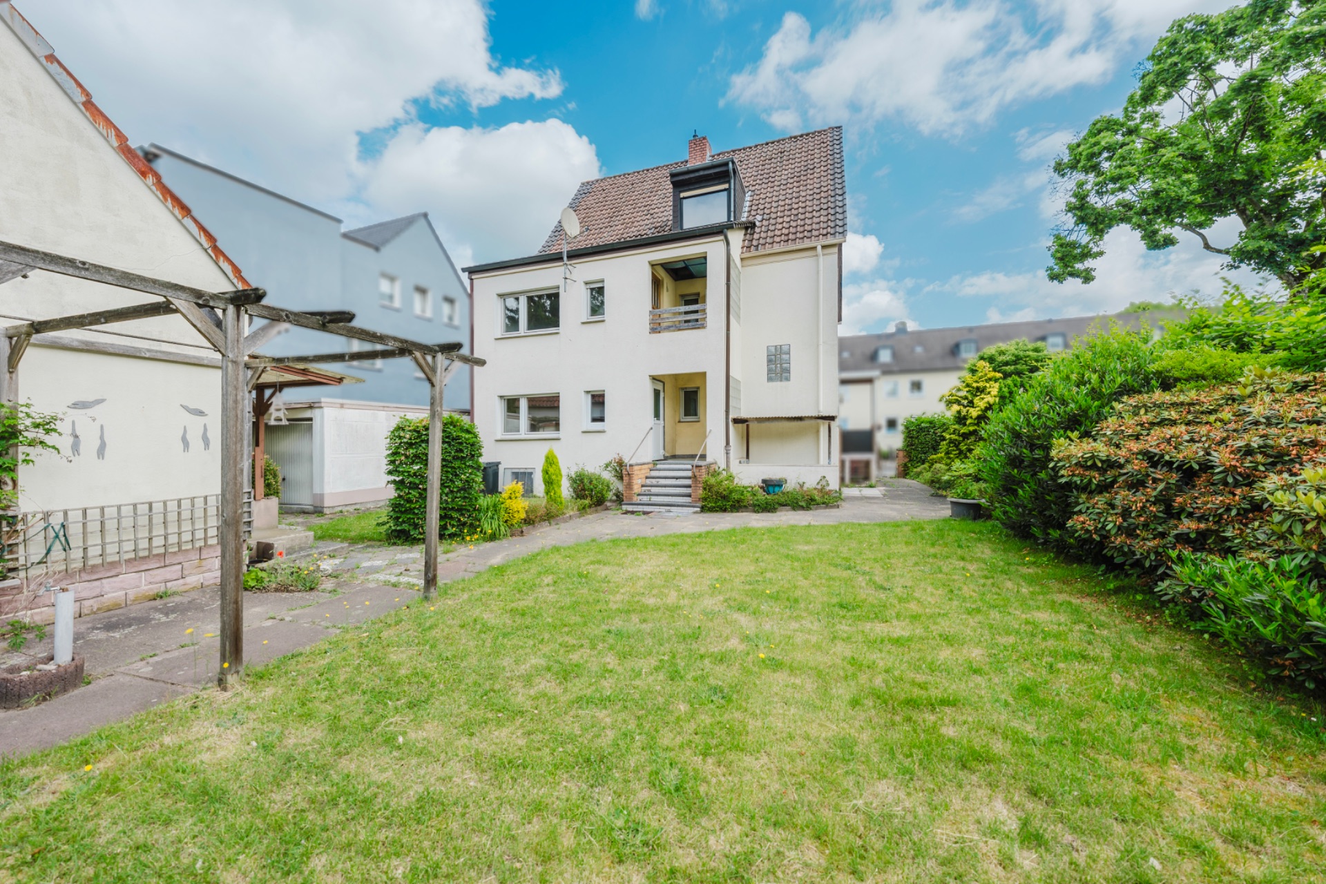 Rückansicht eines weißen Wohnhauses mit Garten und überdachter Terrasse.