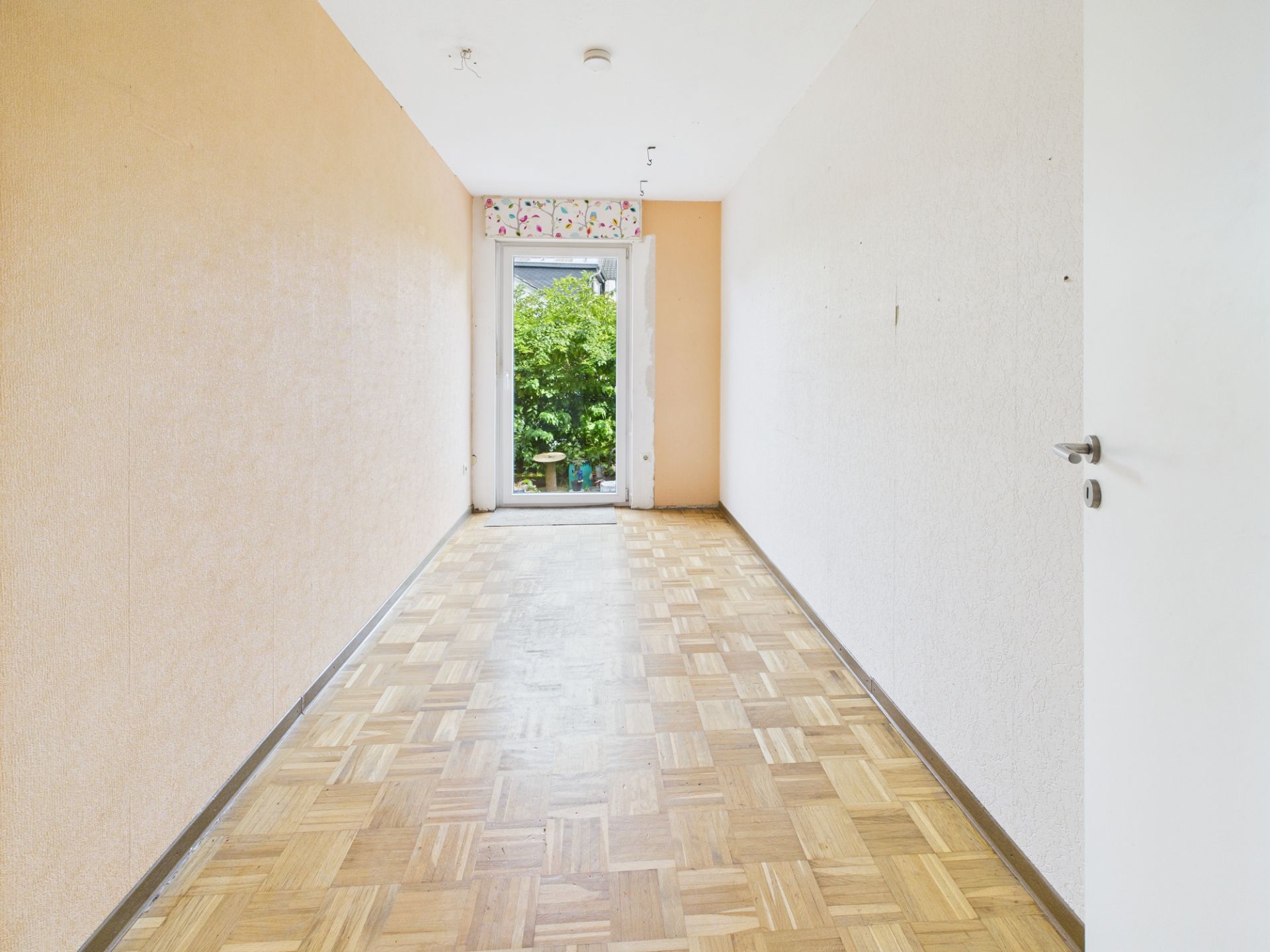 Langer, schmaler Raum mit Parkettboden und Tür zum Garten.