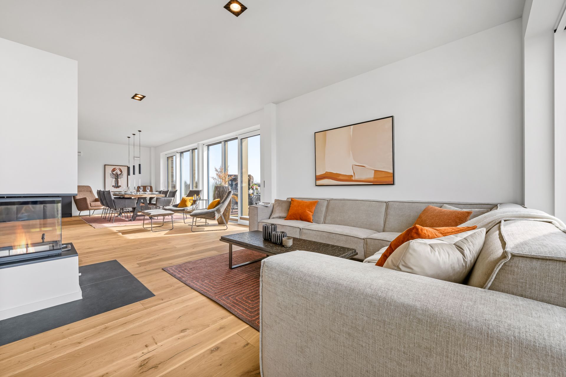 Helles Wohnzimmer mit großem Ecksofa, Kamin und Essbereich, Holzfußboden und Fensterfront.