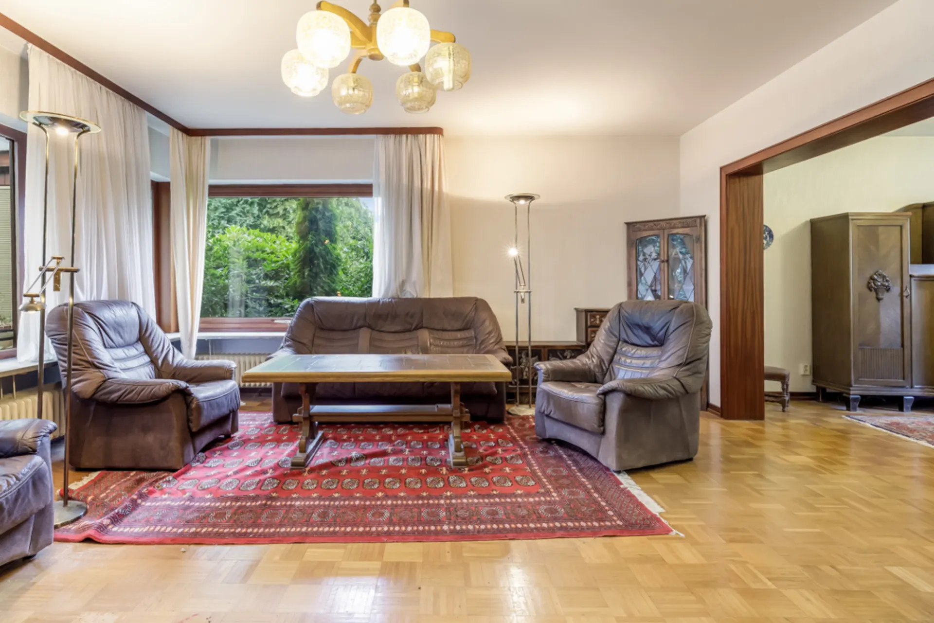 Wohnzimmer mit braunen Ledersesseln, Sofa, Holztisch, Teppich und großer Fensterfront.