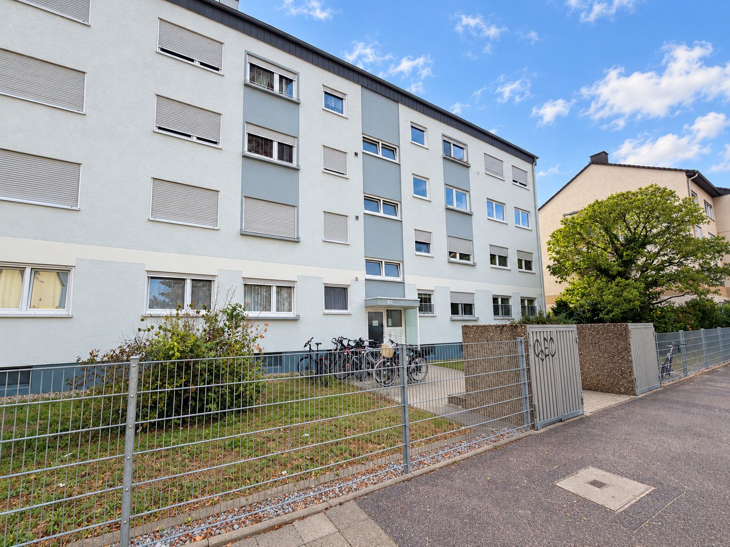 Mehrfamilienhaus mit vier Etagen, Fahrrädern vor dem Eingang und Vorgarten.