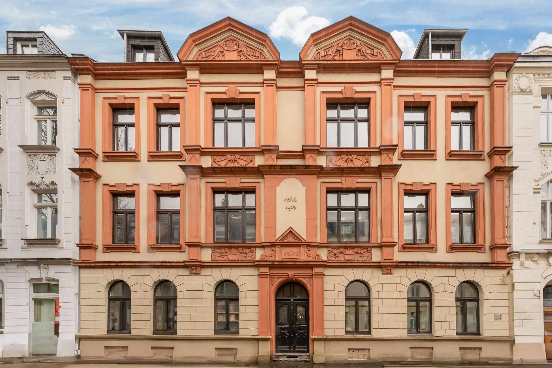 Fassade eines historischen dreistöckigen Wohnhauses mit mehreren Fenstern und verziertem Eingang.