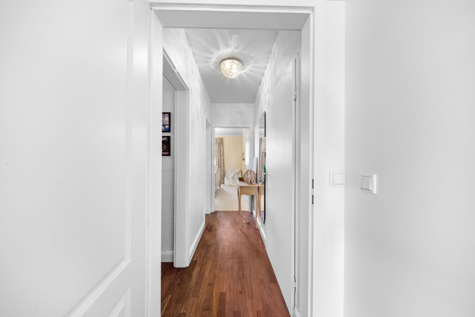 Heller Flur mit Holzfußboden, Türöffnungen und einem Spiegel an der Wand.