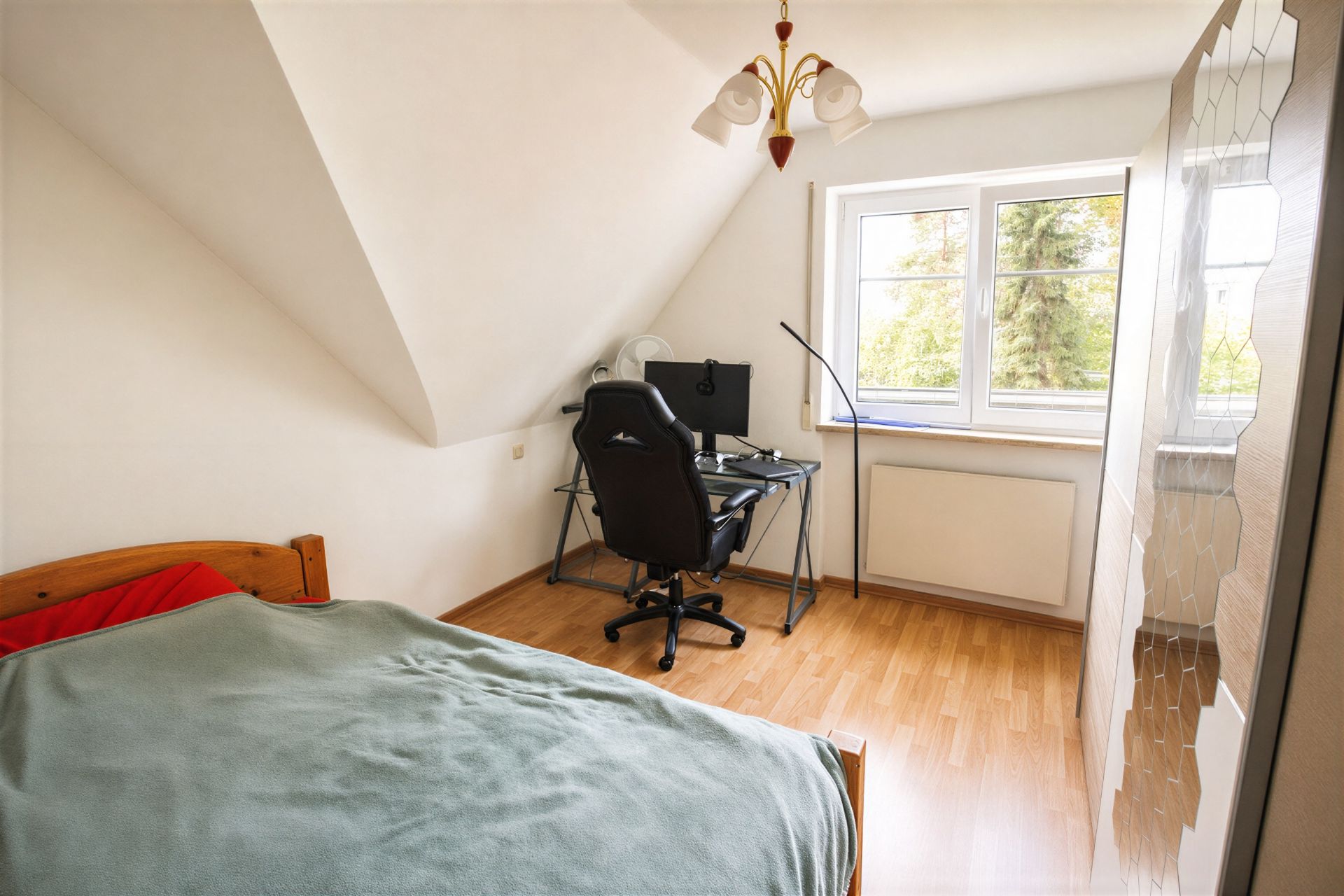 Helles Schlafzimmer mit Schreibtisch, Stuhl, Bett und Fenster mit Blick ins Grüne.