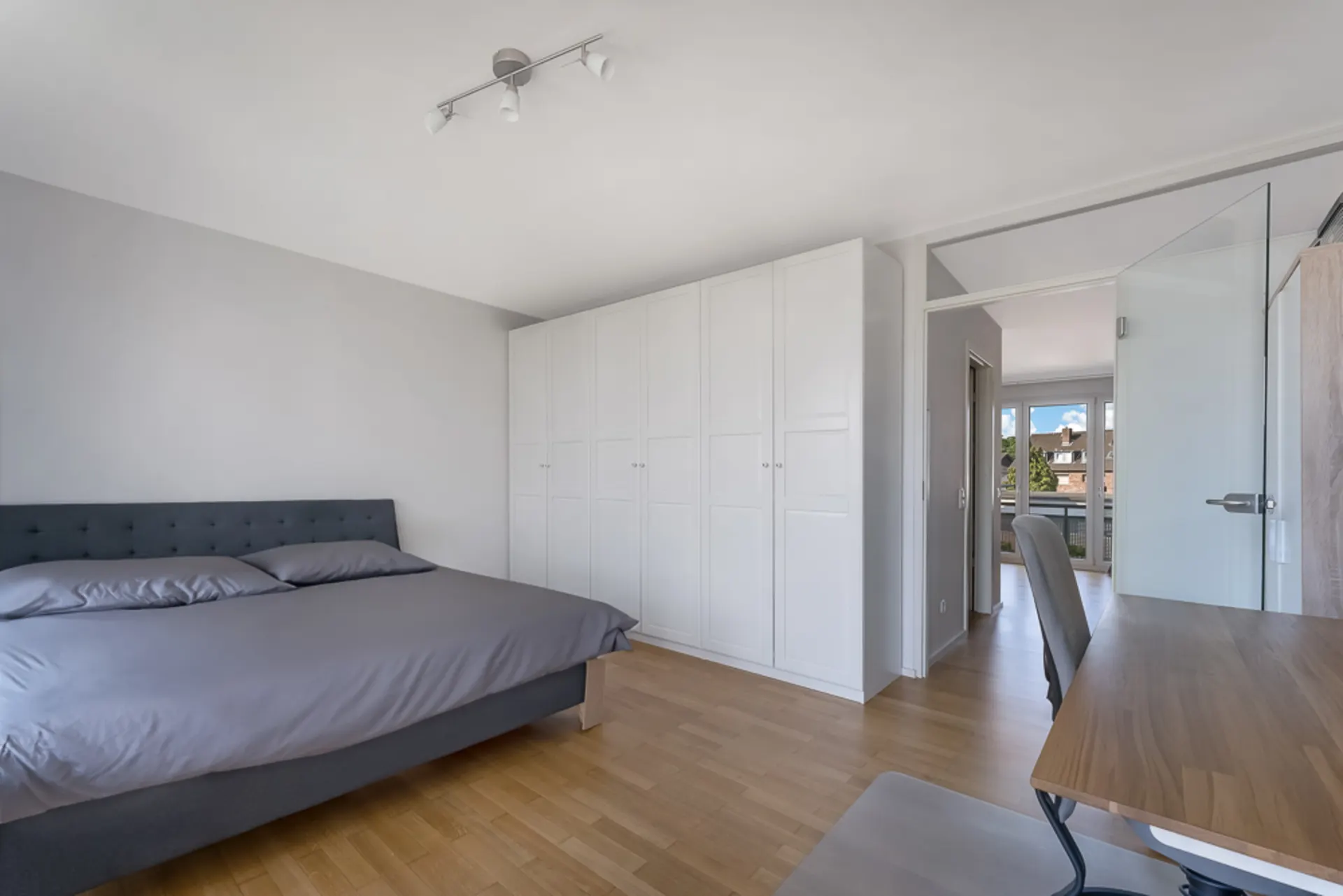 Helles Schlafzimmer mit Doppelbett, großem weißen Kleiderschrank und Schreibtisch aus Holz.