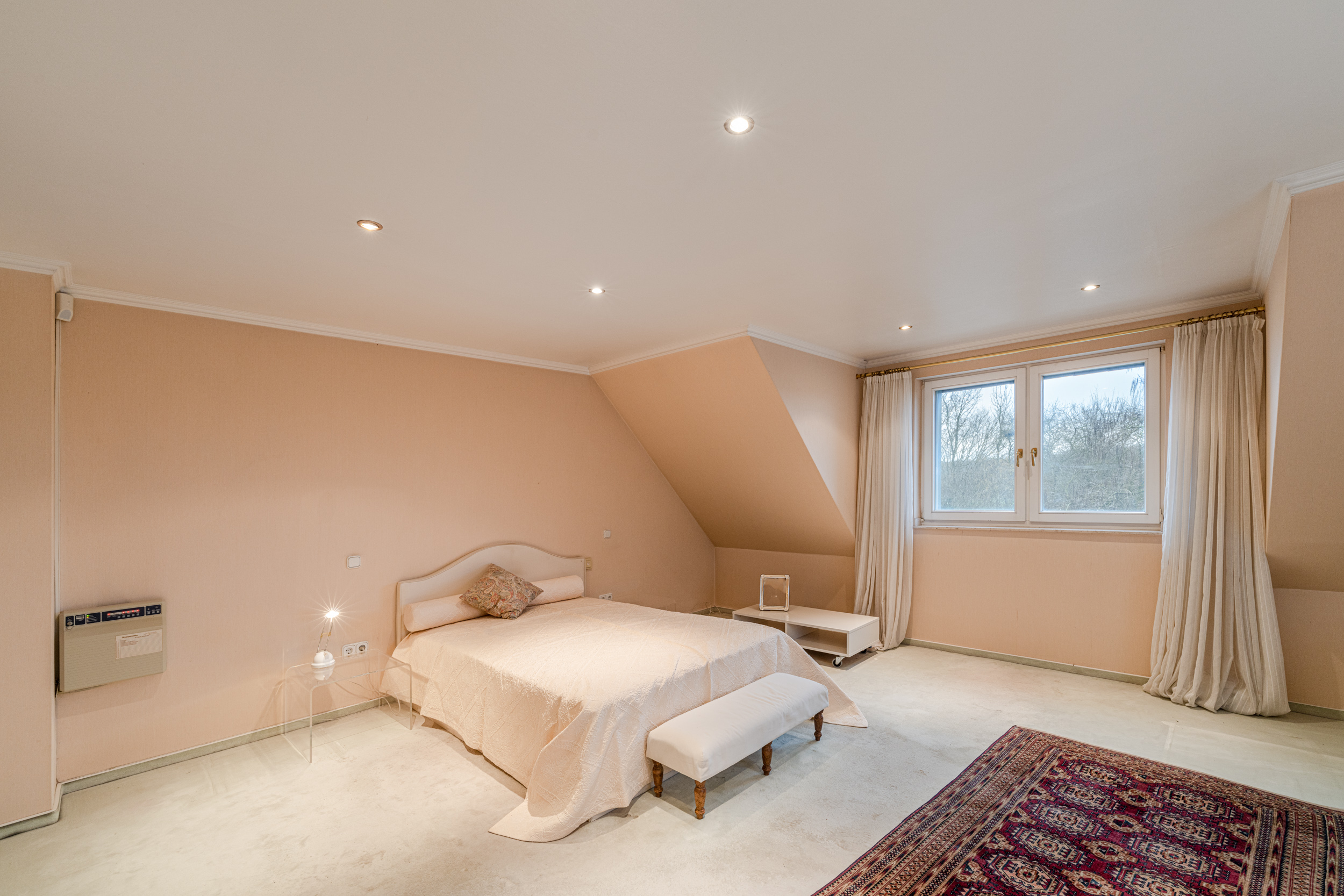 Helles Schlafzimmer mit Doppelbett, Teppich, Fenster und cremefarbenen Wänden.