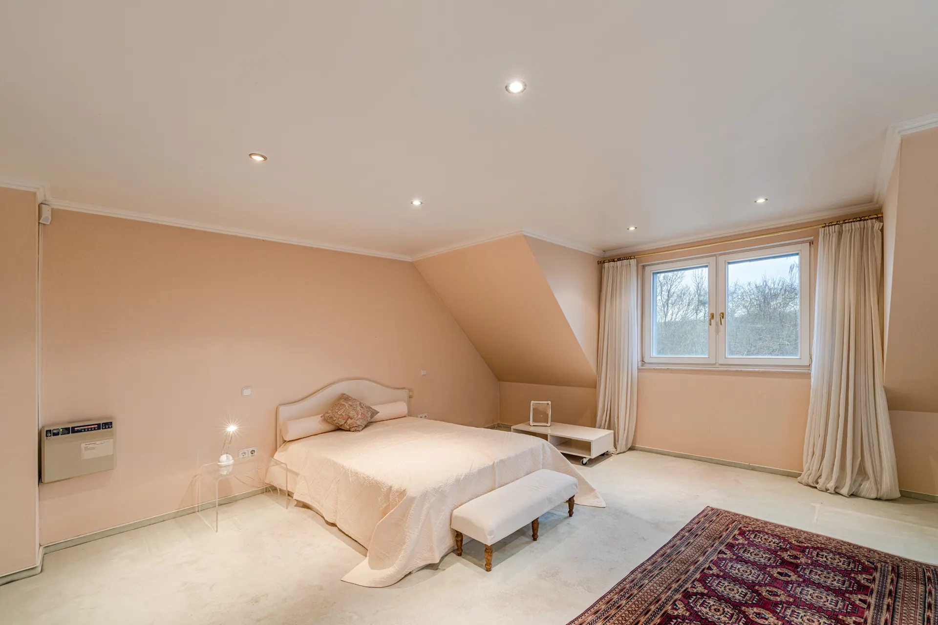 Helles Schlafzimmer mit Doppelbett, Teppich, Fenster und cremefarbenen Wänden.