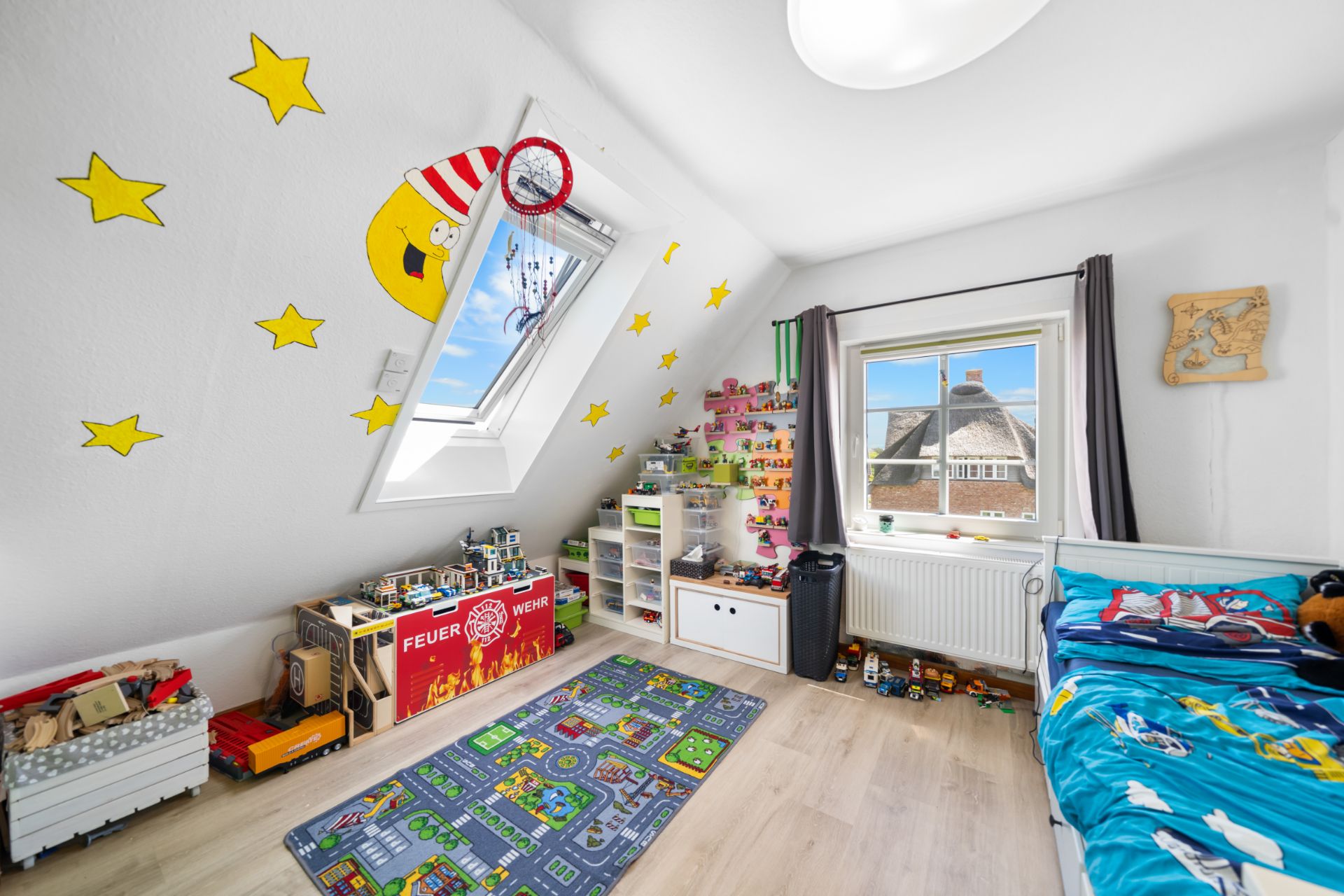 Helles Kinderzimmer mit Spielteppich, Spielzeugregalen, Bett und Wanddeko mit Mond und Sternen.