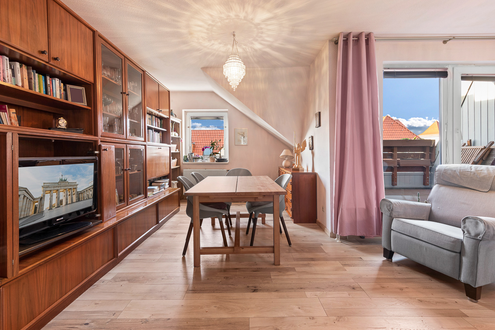 Wohnzimmer mit Holzmöbeln, Esstisch, Regalen, Fernseher und Sessel, Fenster mit Blick nach draußen.