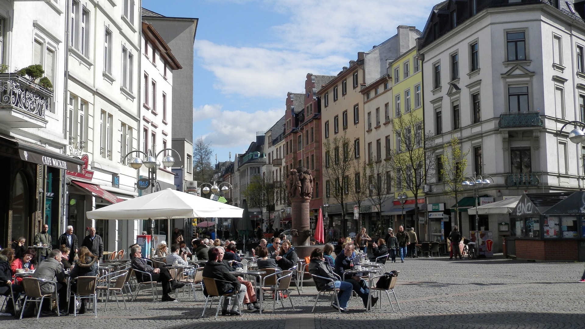 Menschen sitzen an Tischen im Freien vor Wohnhäusern und genießen das Wetter.