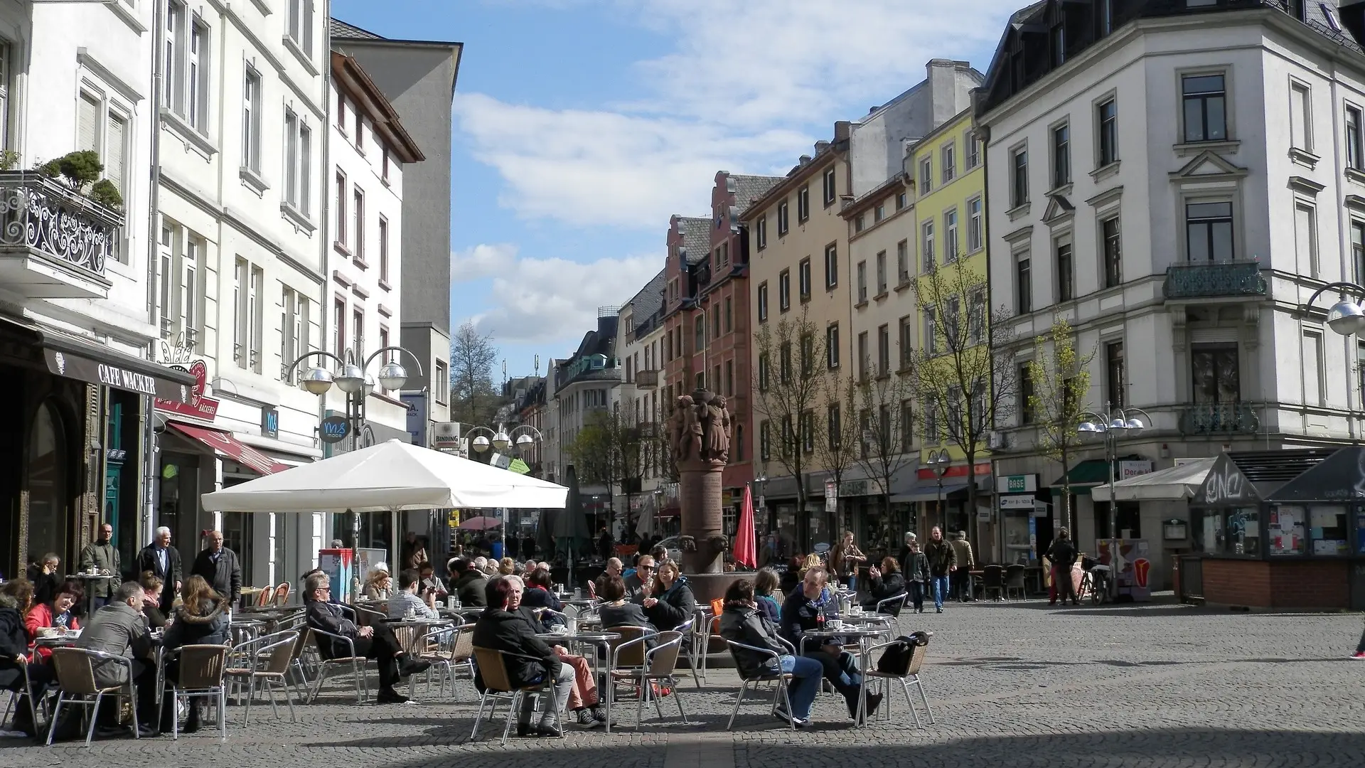 Menschen sitzen an Tischen im Freien vor Wohnhäusern und genießen das Wetter.
