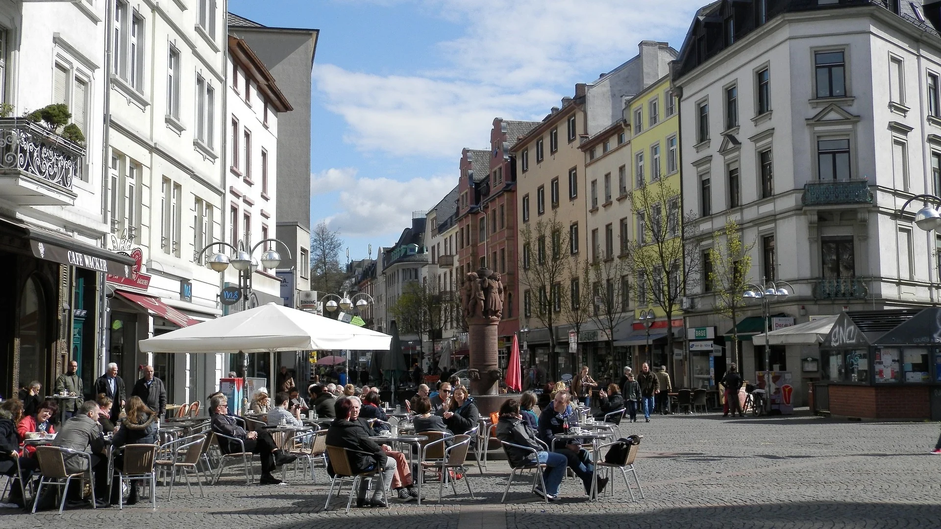Menschen sitzen an Tischen im Freien vor Wohnhäusern und genießen das Wetter.