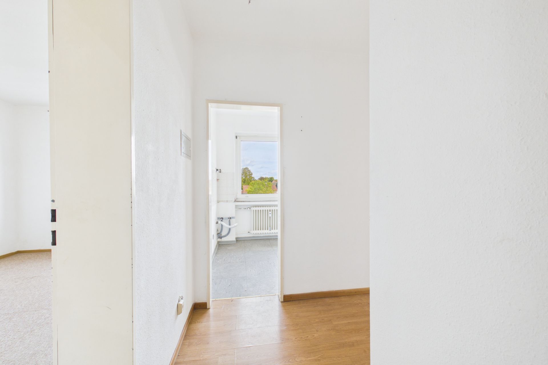 Heller Flur mit Holzboden und Blick in Raum mit Fenster und Heizkörper.