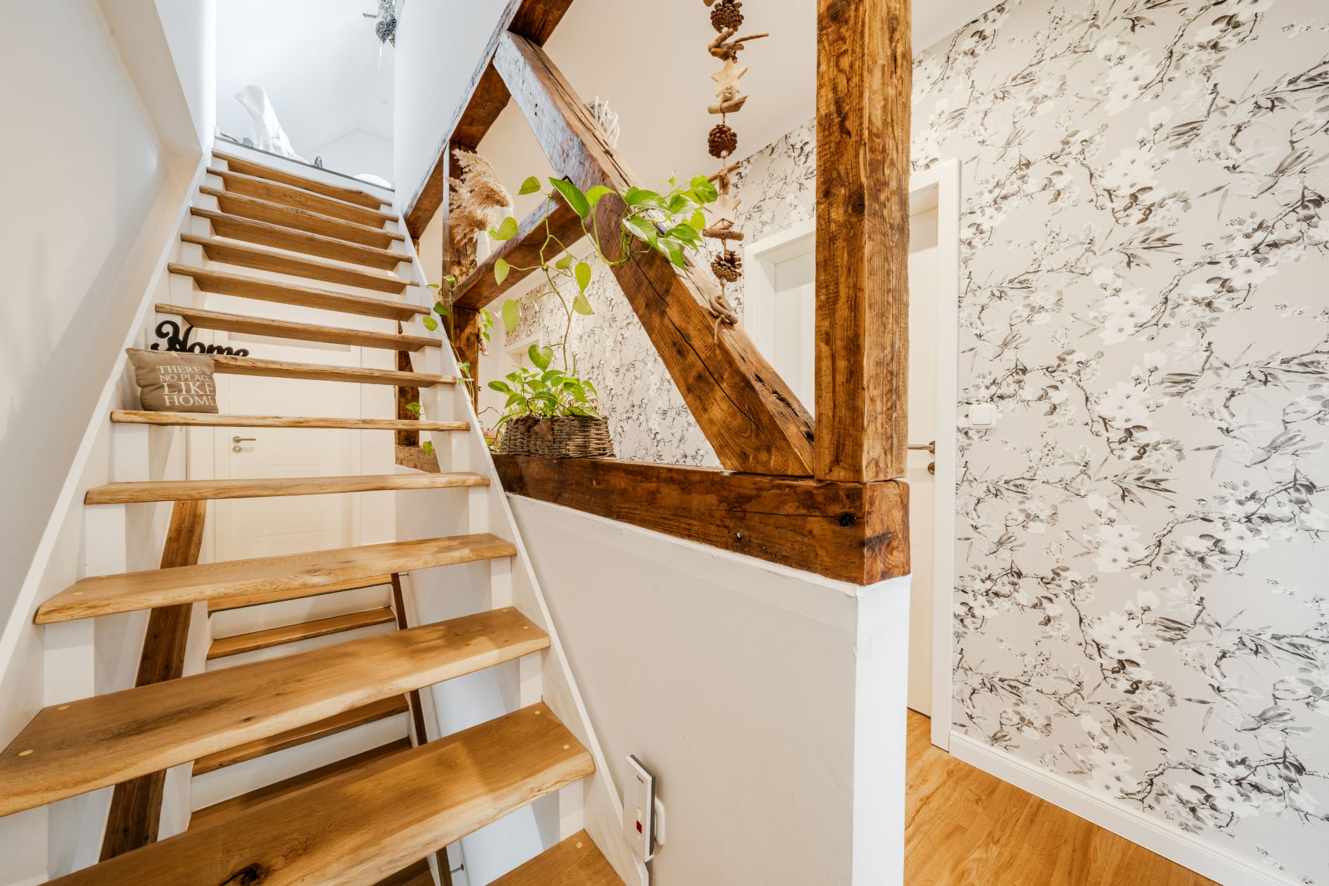 Holztreppe mit Pflanzen und dekorativem Geländer, daneben Flur mit gemusterter Tapete.