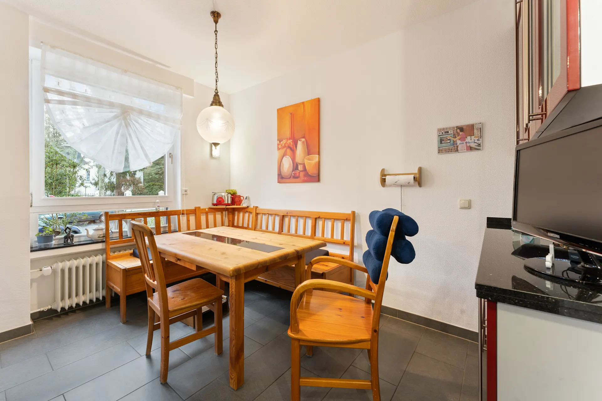 Heller Essbereich mit Holztisch, Eckbank, Stuhl, großem Fenster und Wandbildern.