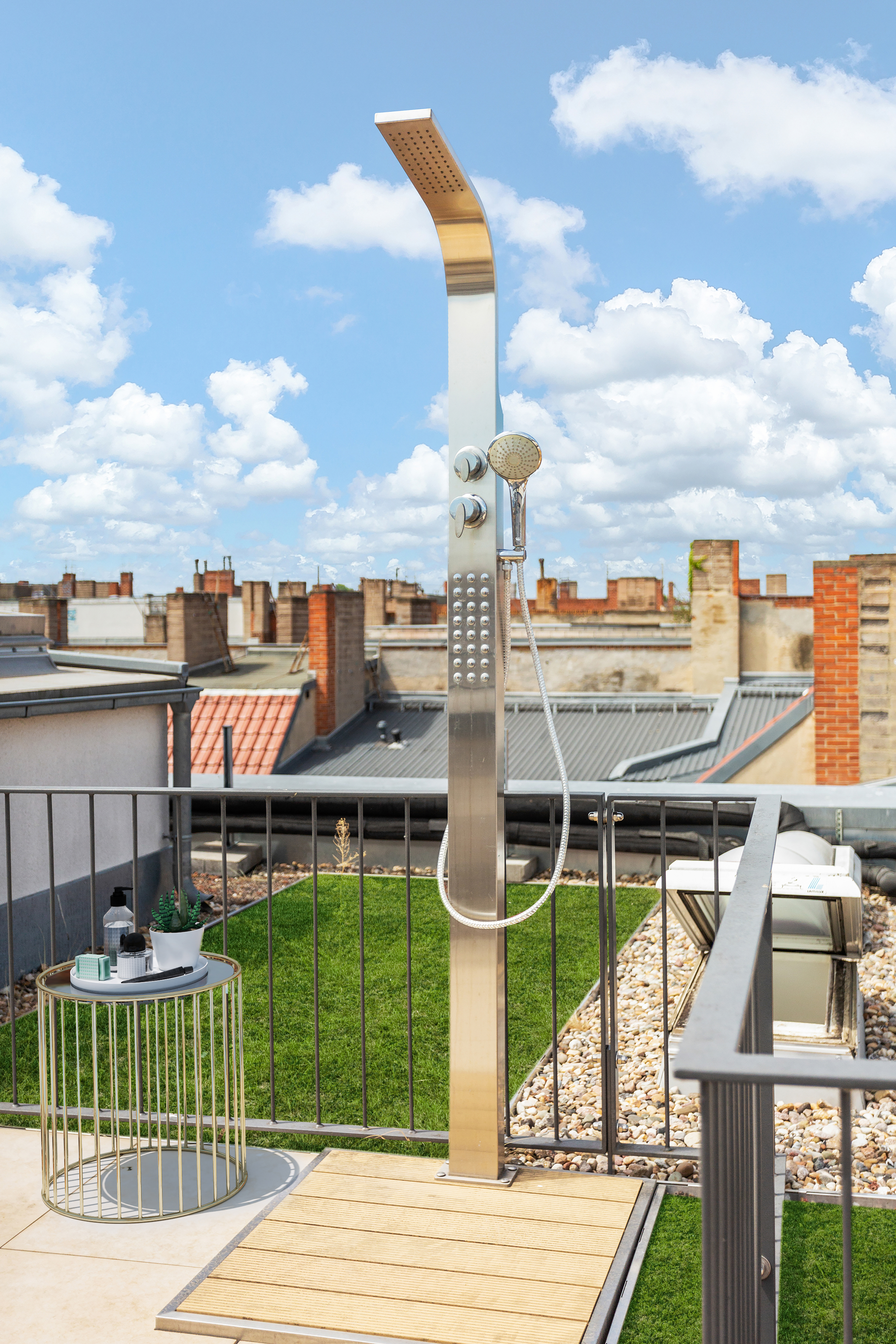 Außendusche auf einer Dachterrasse mit grünem Kunstrasen und kleinem Beistelltisch.