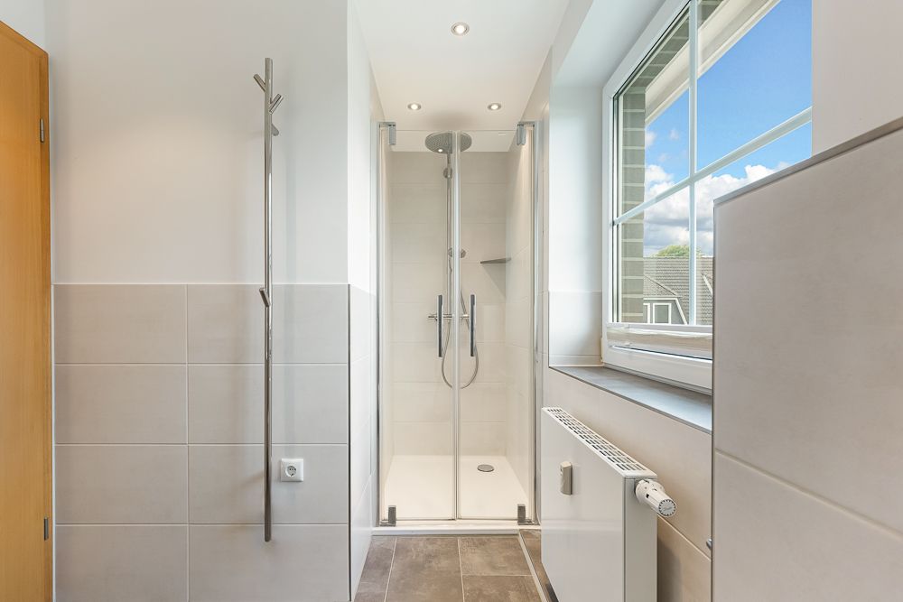 Modernes, helles Badezimmer mit Dusche, Fenster und Handtuchheizkörper.