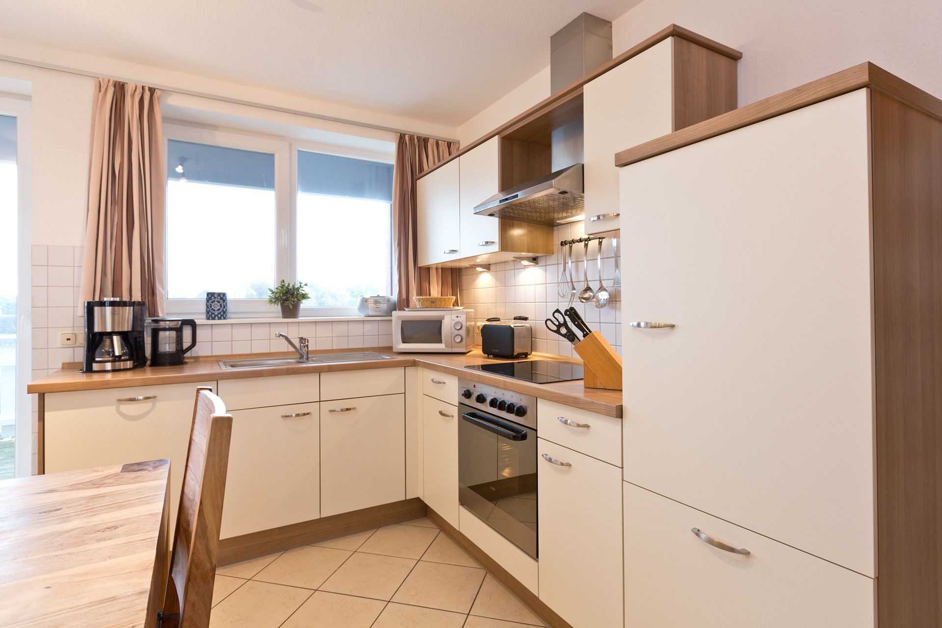 Moderne Einbauküche mit Herd, Backofen, Spüle und Küchengeräten in hellen Farben.