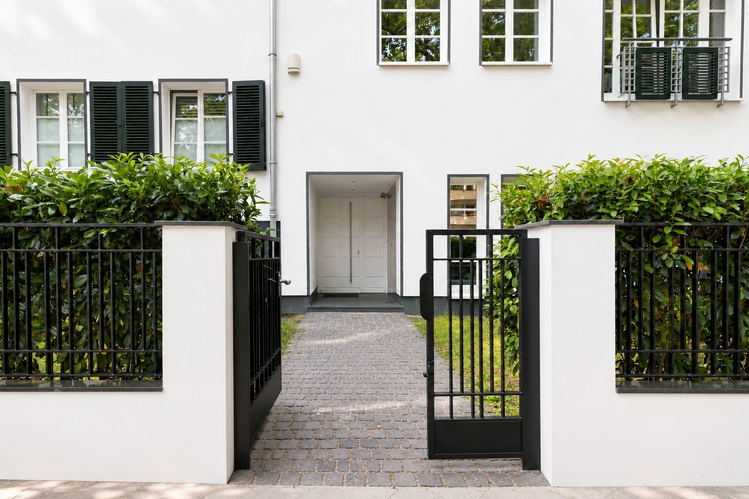 Eingang eines Wohnhauses mit offenem Tor, Hecke und weißen Wänden.