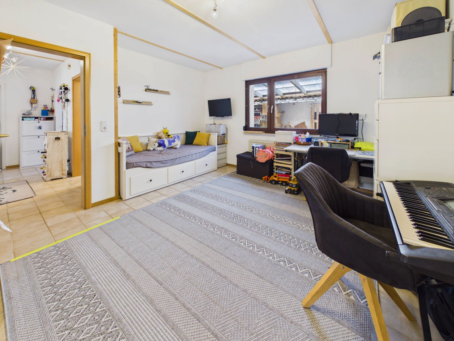 Helles Wohnzimmer mit Sofa, Schreibtisch, Klavier und großem Teppich auf dem Boden.