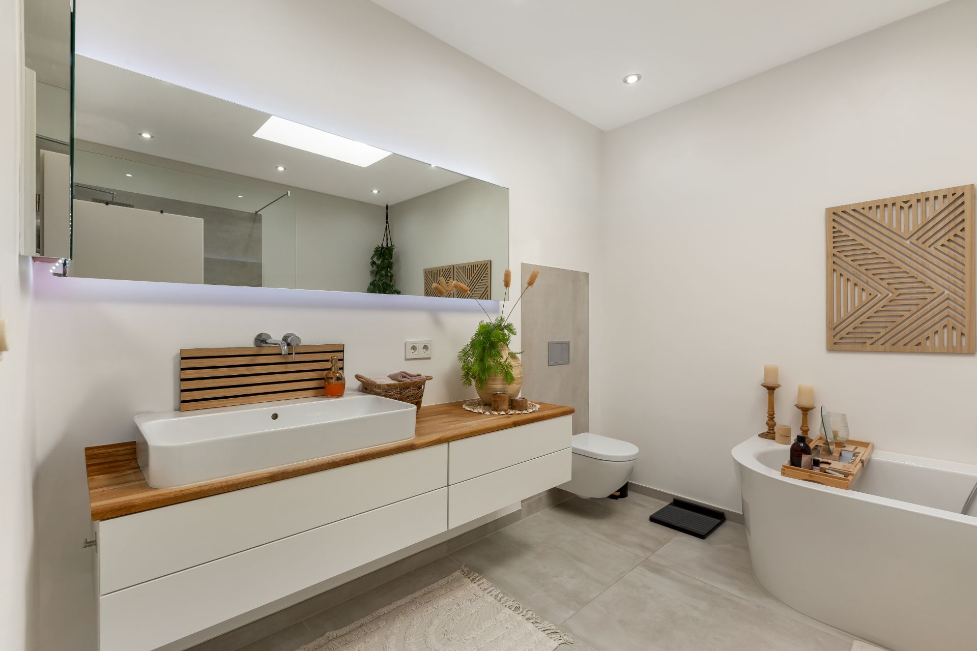 Modernes Badezimmer mit großem Spiegel, Waschbecken, Badewanne und heller Dekoration.