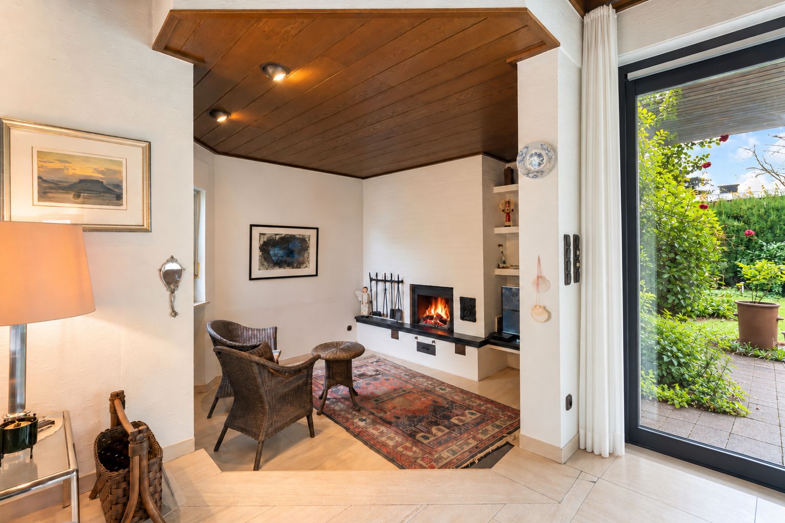 Gemütliche Sitzecke mit Kamin, zwei Stühlen, Teppich und großem Fenster zum Garten.